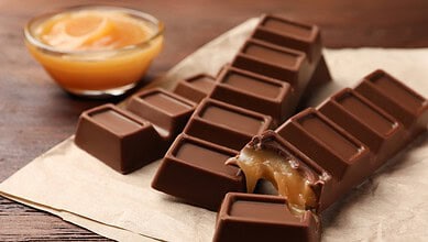 Close-up of a caramel-filled chocolate bar with a piece broken off, revealing the caramel inside.