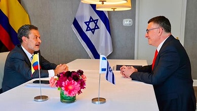 Diplomatic meeting between officials with flags of Colombia and Israel in the background.
