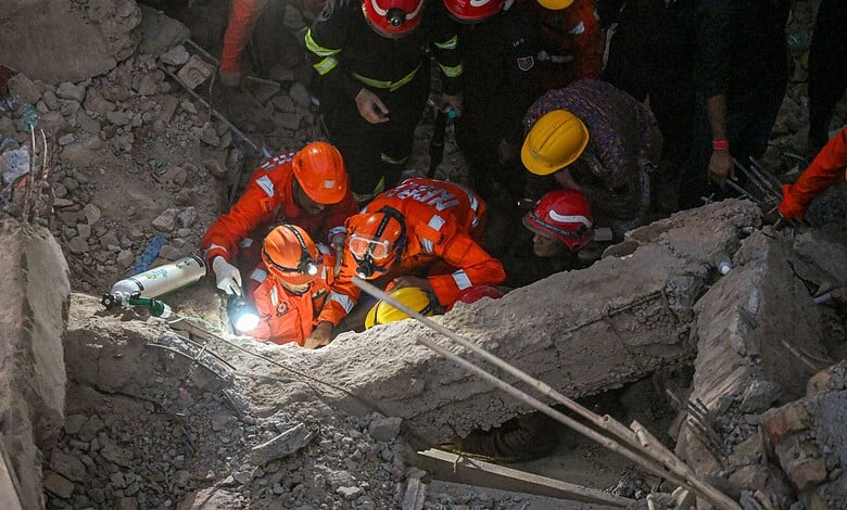 Rescue workers in orange uniforms and helmets working amidst debris after building collapse.