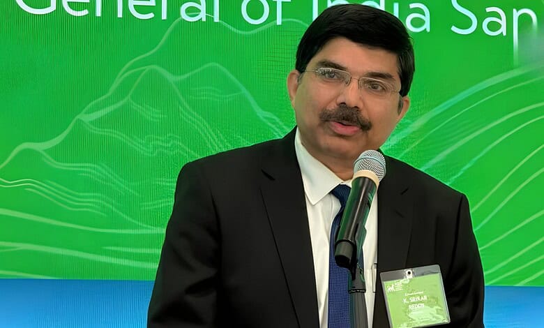 Srikar Reddy speaking at a conference with a green backdrop.