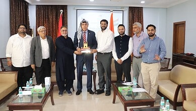 Group of men in formal attire at a meeting, with one man receiving a cake, in Hyderabad.