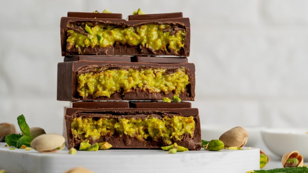 Stacked chocolate bars filled with green pistachio filling on a white surface.
