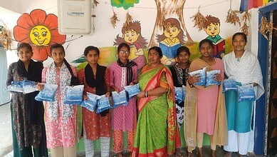 Children at Anganwadi centre holding blue school supplies, with colourful wall art in the background.