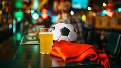 Football, beer, and a red scarf on a bar counter in a lively pub setting.