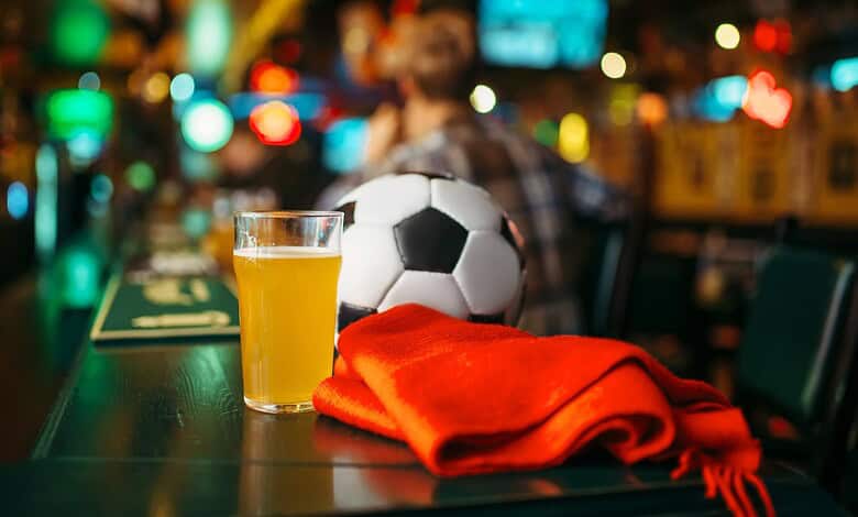 Football, beer, and a red scarf on a bar counter in a lively pub setting.