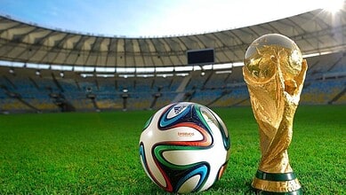 FIFA World Cup football and trophy on a stadium field under bright sunlight.