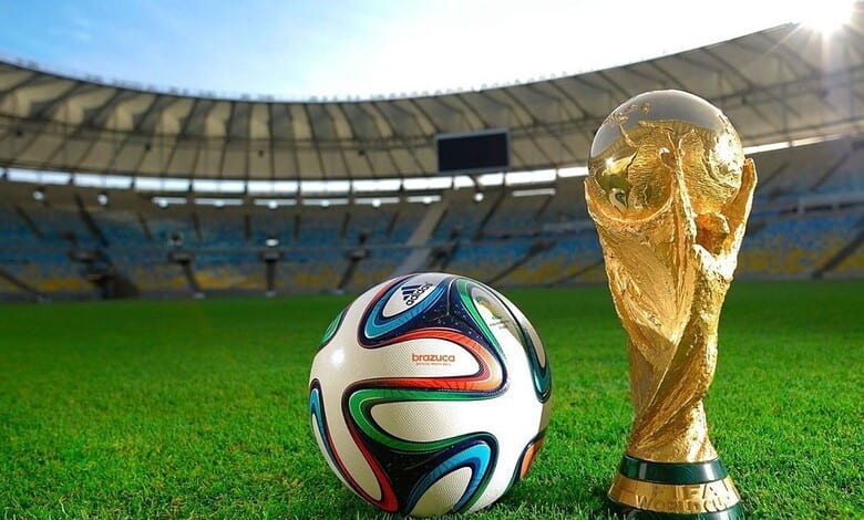 FIFA World Cup football and trophy on a stadium field under bright sunlight.