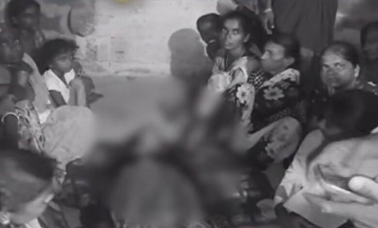 Group of villagers gathered around a person in distress in a rural setting.