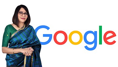 Indian woman in green saree standing next to Google logo, smiling at camera.