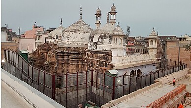 Historic temple with domes and minarets in an urban setting, surrounded by a fence.
