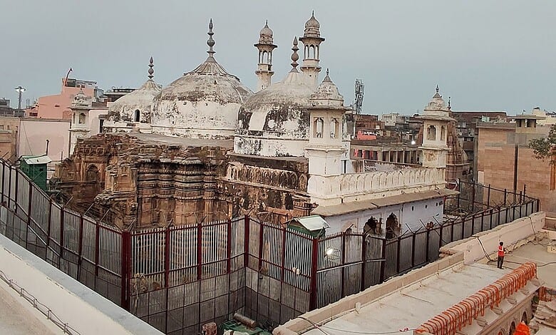 Historic temple with domes and minarets in an urban setting, surrounded by a fence.
