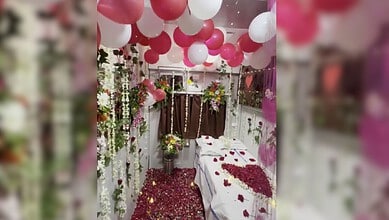 Honeymoon suite decorated with pink and white balloons, flowers, and rose petals on the bed.