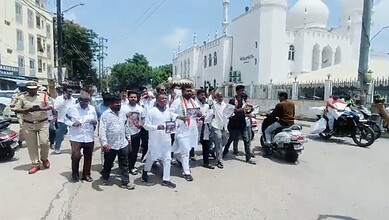 Group of people walking on street near a white mosque with domes and minarets in the background.