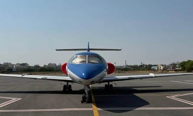 Small private jet on runway with cityscape in background, clear sky, daytime.