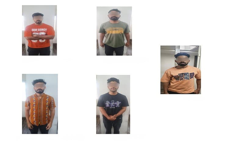 Group of five men with blurred faces, wearing casual T-shirts and standing indoors.