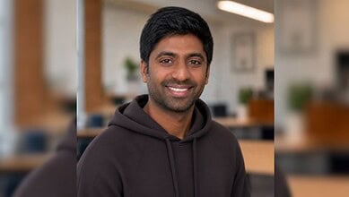 Smiling Indian man in a black hoodie in an office setting.