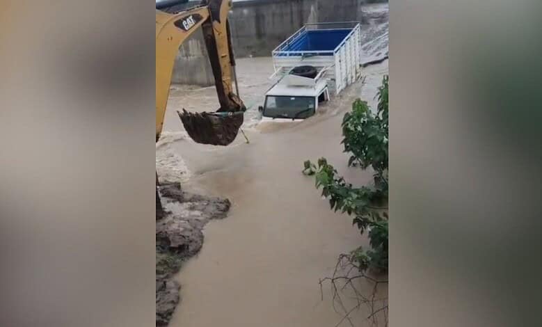 Flooded street with a construction excavator and a white truck submerged in water.