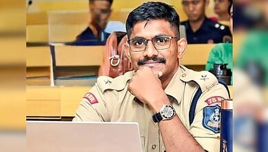 Trainee IPS officer in judicial custody, wearing uniform and glasses, sitting in court.