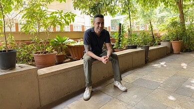 Imran Khan sitting on a ledge in a garden with potted plants and trees.