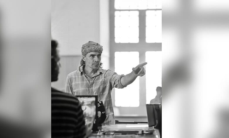 Imtiaz Ali gesturing passionately during a film scene in a bright room.