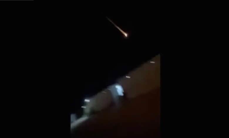 Bright meteor streaks across a dark night sky over a cityscape.