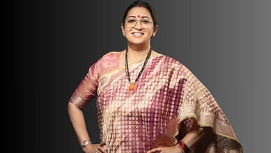 Smriti Irani smiling in traditional saree with jewelry and glasses, posing confidently.