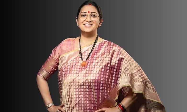 Smriti Irani smiling in traditional saree with jewelry and glasses, posing confidently.