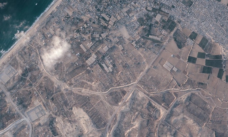 Aerial view of a large earthen barrier construction inside Gaza, with surrounding fields and urban areas.