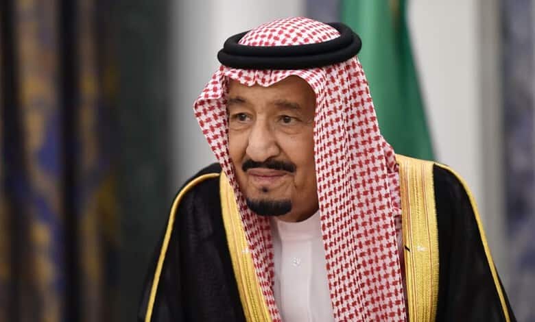 Saudi official in traditional attire at a formal event with green and gold background.