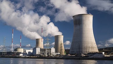 Nuclear power plant with cooling towers emitting steam against a cloudy sky.