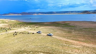 Scenic view of a large water body near Hyderabad, called 'Ladakh of Telangana', with vehicles and grazing.