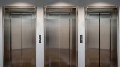 Three elevator doors with control panels in a modern building.