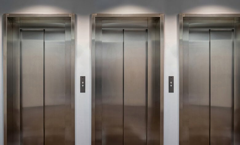 Three elevator doors with control panels in a modern building.