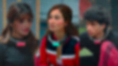 Three women engaged in conversation, blurred background, vibrant clothing, outdoor setting.
