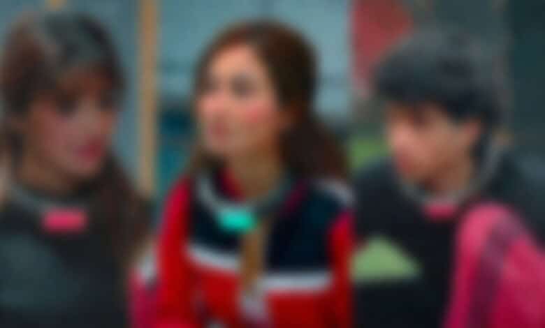 Three women engaged in conversation, blurred background, vibrant clothing, outdoor setting.