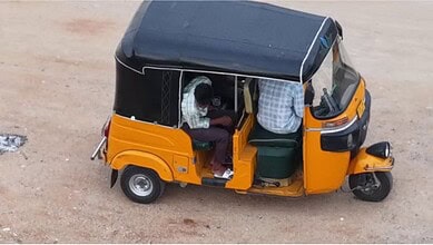 Yellow auto rickshaw parked on a dirt road with two passengers inside.