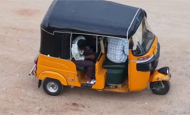 Yellow auto rickshaw parked on a dirt road with two passengers inside.