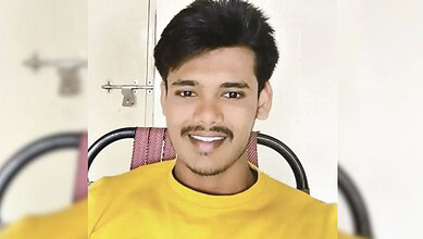 Smiling young man in yellow shirt sitting on a chair indoors.