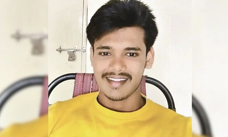 Smiling young man in yellow shirt sitting on a chair indoors.