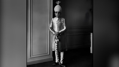 Azam Jah in traditional attire with turban, standing indoors in black and white.