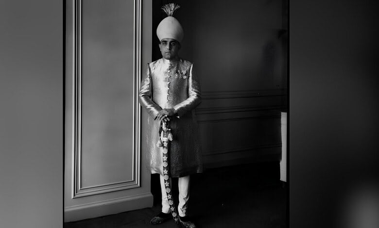 Azam Jah in traditional attire with turban, standing indoors in black and white.