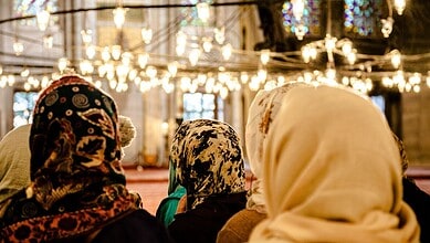 Muslim women wearing hijabs inside a mosque, engaged in prayer or reflection.