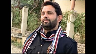 Man with beard and scarf outdoors, looking to the side, in a casual setting.
