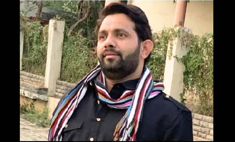 Man with beard and scarf outdoors, looking to the side, in a casual setting.