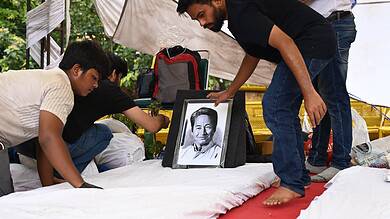 People paying tribute at a memorial with a framed black-and-white photo of a man.