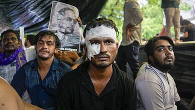 Protesters with bandaged face at a rally, holding a portrait of a leader, under a tent.