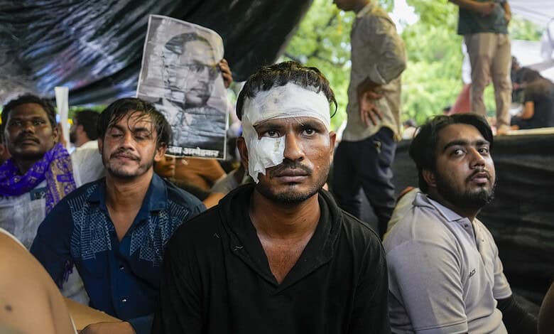 Protesters with bandaged face at a rally, holding a portrait of a leader, under a tent.
