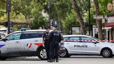 Two police officers standing near police cars on a city street in Paris.