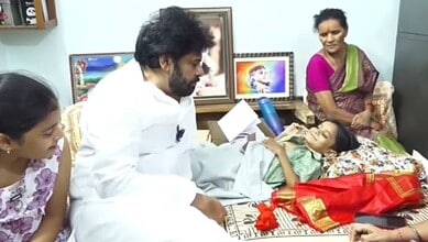 A woman lying on a bed with a microphone, surrounded by family members in a hospital room.