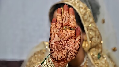 Close-up of a bride's hand with intricate henna designs and gold jewelry.
